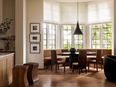 A cozy modern kitchen featuring a built-in bench seating area with a wooden table and chairs, situated under a large bay wind