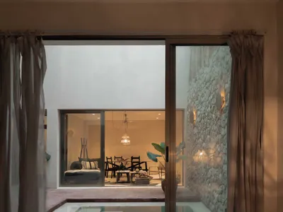 A modern bedroom with a concrete wall, a plunge pool, and a see-through glass wall that leads to a living area with a stone w