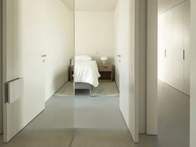 一間簡約臥室，單人床置於水泥地板上，白牆搭配木製床頭櫃。