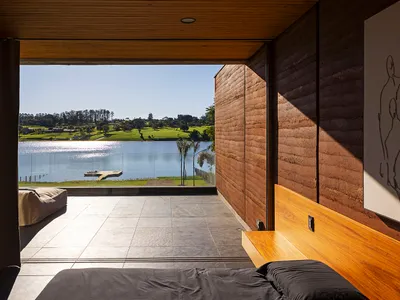 A minimalist bedroom featuring a black bedspread and a wooden headboard, with a view of a lake.