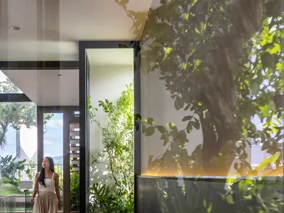 A minimalist bedroom featuring greenery, with a person walking through the space.