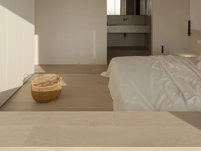 A minimalist bedroom with a wood floor, white walls, and a bed with white sheets.
