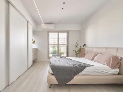 A neutral-colored minimalist bedroom with a upholstered bed, grey blanket, and pink pillows.
