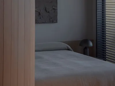 Minimalist bedroom with concrete walls, a simple bed, and a window with blinds.
