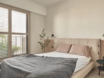 A minimalist bedroom featuring a bed with a fabric headboard, wooden furniture, and a metal bedside table.