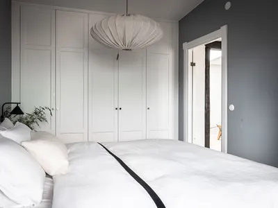 Modern, minimalist bedroom with white bedding, large window, and large white wardrobe.