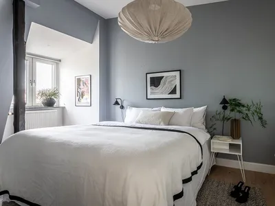 A minimalist bedroom with a white bed, white walls, and a wooden floor.