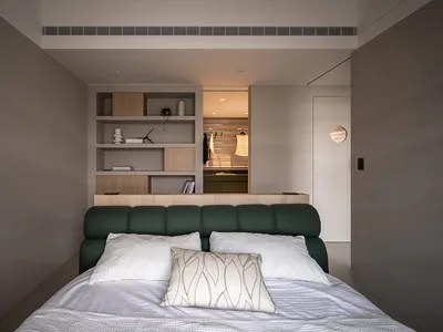 A modern minimalist bedroom featuring neutral materials and a white bed with a green upholstered headboard.