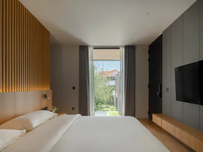 Clean and minimal bedroom with a bed, window, and wooden headboard.