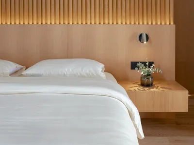 A modern minimalist bedroom featuring a wooden texture headboard and bed frame, with a white duvet and pillows.