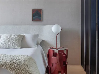 A modern bedroom featuring a contemporary bed with neutral-toned bedding and a unique, burgundy side table.