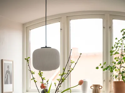 A cozy kitchen scene featuring a ceramic vase with branches and tulips, a mix of ceramic dishes, and soft lighting from a pen