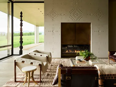 A modern industrial living room with a fireplace, leather chairs, and concrete walls.