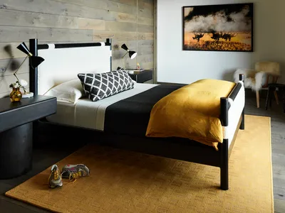 A minimalist bedroom with a wooden bed, white and yellow linens, and a textured rug.