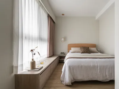 A minimalist bedroom with a wooden bed and wooden storage bench alongside the window, featuring sheer and light-colored curta