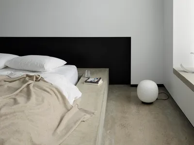 A minimalist bedroom with a concrete floor, wood headboard, and clean, simple design.