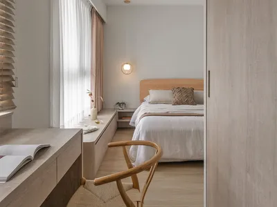 Minimalist bedroom with a wooden bed frame, white bedding, and a woven chair.