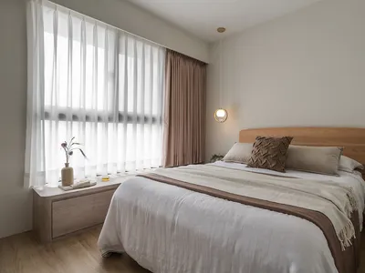 A minimalist bedroom with a light-colored bed, white and brown curtains, and a wooden headboard.