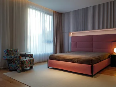Interior design of a minimalist bedroom featuring a bed with a large burgundy headboard and an armchair with a geometric prin