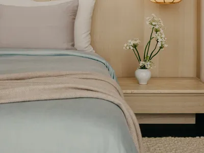A minimalist bedroom with a bed, pillows, and a hanging lamp with flowers on a nightstand.