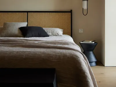 A minimalist bedroom with a wooden headboard and a bed with clean lines, accompanied by a hanging lamp and a bedside table.