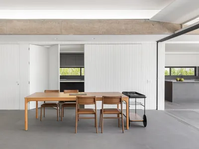 A modern minimalist kitchen with wooden table, brown chairs, and metal cart.