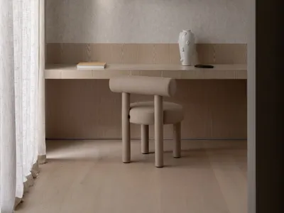 Photograph of a minimalist bedroom featuring wooden furniture and a white vase.