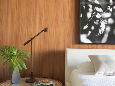 A modern minimalist bedroom featuring a nightstand with a potted indoor plant, a reading lamp, books, and a framed black and