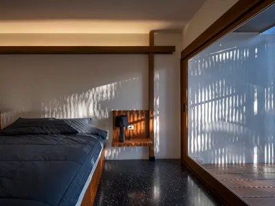 Modern minimalist bedroom with dark blue bedding, wooden headboard, and concrete floor.