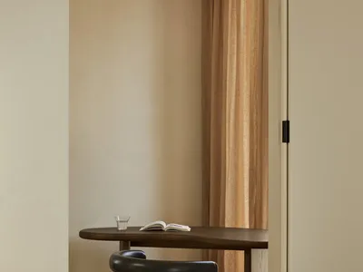 A minimalist home office featuring a wooden table with a glass of water and an open book, accompanied by a comfortable black