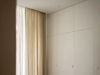 Modern minimalist bedroom featuring a bed with white sheets and curtains made of light-colored fabric, against a wall with a