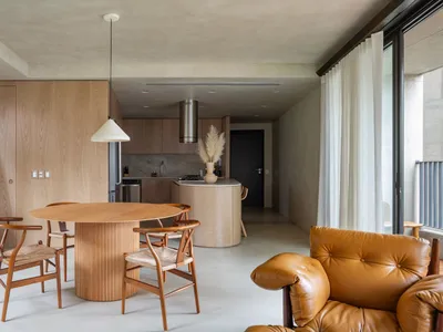 A modern, minimalist residential kitchen with a round dining table and wooden furniture.
