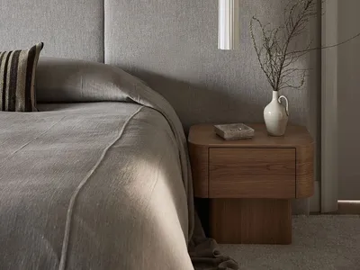 Minimalist bedroom featuring a grey upholstered bed and wooden nightstand with a vase and plant.