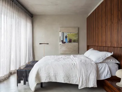 Minimalist bedroom with a white bed and wooden walls. The room features simple, clean lines and a serene atmosphere.