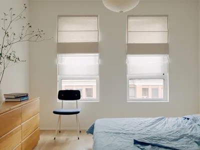 A minimalist bedroom featuring a wooden floor, a blue bedspread, and a black chair.