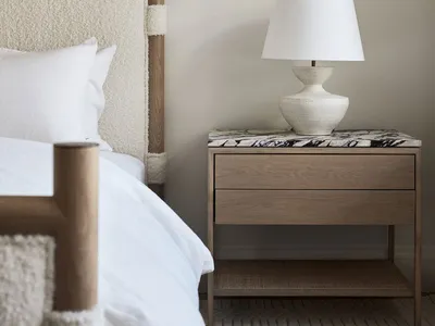 A modern, minimalist bedroom featuring a bed with a wooden headboard, marble accents, and a textured blanket.