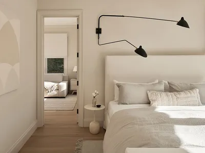 A modern minimalist bedroom with a simple white bed, white linens, and a soft fabric headboard.