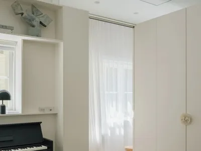 A minimalist bedroom with neutral-colored walls and furniture, featuring a black piano and green cushions.