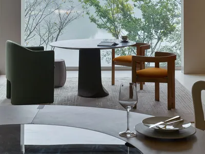 A modern restaurant with a round table and chairs next to large windows overlooking water and trees.