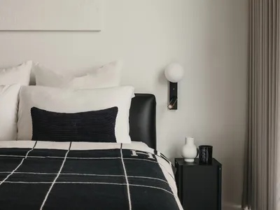 A minimalist bedroom featuring a black and white checkered blanket, a white pillow, and a leather bedframe.