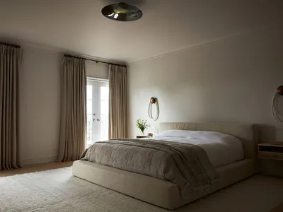 A minimalist bedroom with grey textiles and a neutral color palette, featuring a large bed with a beige headboard, a modern l
