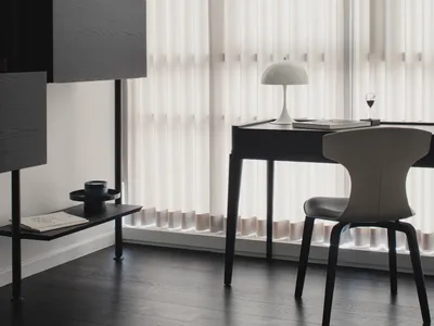 A modern, minimalist home office featuring a sleek desk, chair, and shelving unit with neutral colors and a large window with