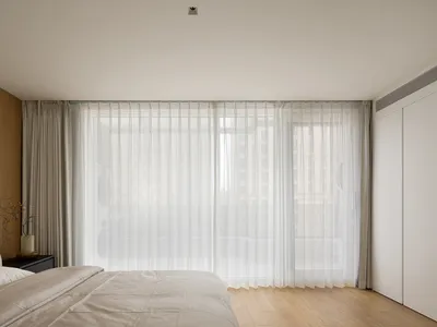 A minimalist bedroom with a large window covered by sheer white curtains.