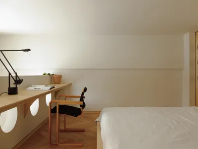A minimalist bedroom with a wooden bed, desk, and chair