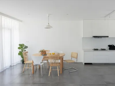 A sleek, modern minimalist kitchen with concrete flooring and white cabinets, featuring a wooden dining table and chairs.