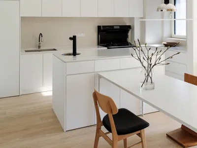 A minimalist kitchen with white cabinets, a hanging glass pendant light, and a light wood floor.