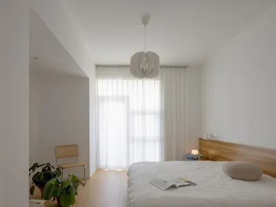 A minimalist bedroom with white bedding, wood flooring, and white lighting fixtures.