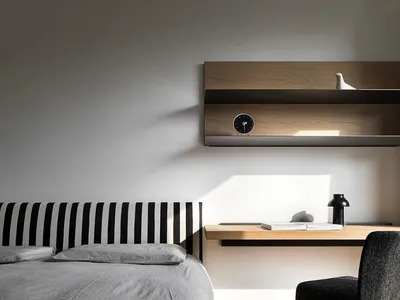 Modern minimalist bedroom featuring a bed with a black and white striped headboard and a light wood desk with a clock on it.