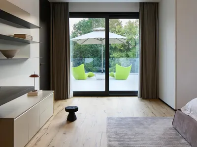 A modern bedroom with white cushions, wooden flooring, and floor-to-ceiling windows.