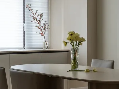 Modern dining room with minimalist furniture and decor, including a round table, chairs, and fresh flowers in a vase by the w